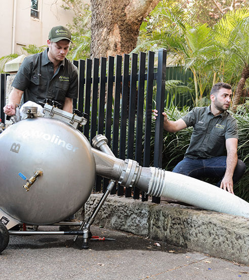 Two Relining Company employees using a machine to fix an outdoor drain