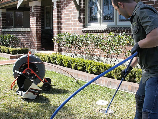 A pipe relining employee cleaning an outdoor drain