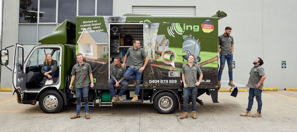 Pipe Relining Employees standing outside the Relining Truck looking happy