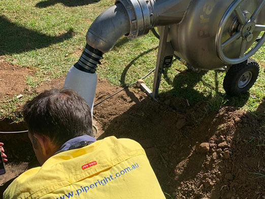 A pipe relining employee in the dirt next to a pipe machine