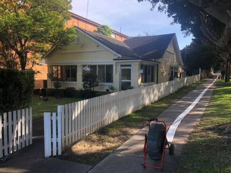 A house with a picket fence and a pipe relining machine on the sidewalk