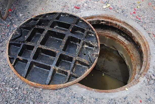 Partially open blocked drain on a street with water/sewage visible below