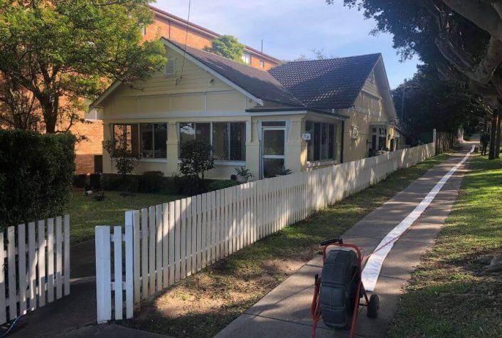 A house with a picket fence and a pipe relining machine on the sidewalk